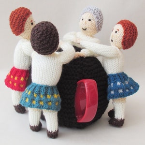Puede incluir: Cuatro muñecas de punto de diferentes colores y atuendos están sentadas alrededor de una taza negra con una asa roja. Las muñecas llevan faldas con diferentes patrones.