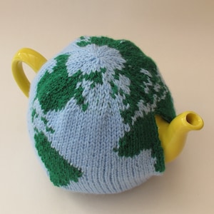 May include: A blue and green knitted teapot cozy with a world map design. The cozy is on a yellow teapot.