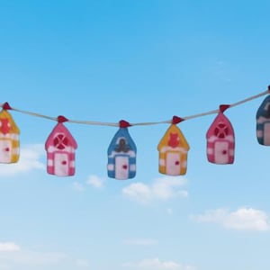 May include: A garland of small, house-shaped decorations in various colours, including yellow, pink, and blue, against a blue sky. Each house has a different colour scheme, with red accents. The houses are strung on a thin, white string.