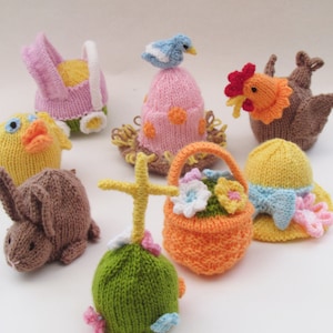 May include: A collection of knitted Easter egg decorations, including a chick, a bunny, a basket of flowers, a cross, a bird in a nest, a rooster, and a carriage. The decorations are all made with colourful yarn and have a whimsical, handmade look.