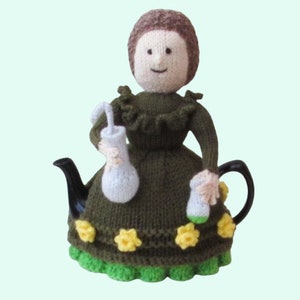 May include: A knitted tea cosy in the shape of a woman in a green dress, holding two white and cream-coloured accessories. The dress features yellow flower accents and a green trim. The cosy is placed on a black teapot.