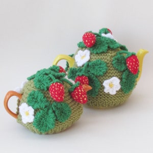 Peut inclure: Deux chauffe-théières en crochet de couleur verte avec des fleurs blanches et des fraises rouges. Les chauffe-théières sont conçues pour s'adapter à une théière.