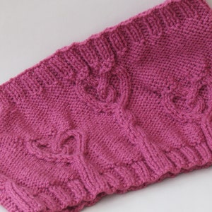 May include: A pink knitted headband with a cable knit pattern. The headband is folded in half and has a soft, textured surface.