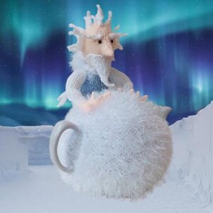 Peut inclure: Une théière tricotée blanche et duveteuse en forme de personnage avec une barbe et un visage. L'image présente un paysage enneigé et des aurores boréales en arrière-plan. La théière a une anse.