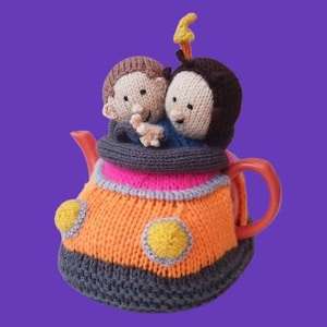 May include: A knitted teapot cosy with two small figures on top. The cosy is mainly orange with grey and yellow details, a pink band, and a grey collar. The teapot has a red handle and spout, set against a purple background.