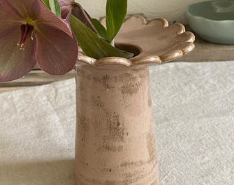 Può includere: Un vaso in ceramica rosa chiaro con bordo smerlato e finitura testurizzata usurata. Il vaso ha un corpo cilindrico che si allarga leggermente verso l'alto e contiene un fiore di elleboro viola scuro con foglie verdi e un piccolo stelo.