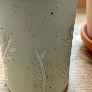 Pu&ograve; includere: Un bicchiere in ceramica beige con interno bianco ed esterno strutturato. Il bicchiere presenta un design a foglie intagliate. La superficie macchiata aggiunge un tocco rustico alla ceramica fatta a mano. Il bicchiere &egrave; adatto per bevande calde o fredde.