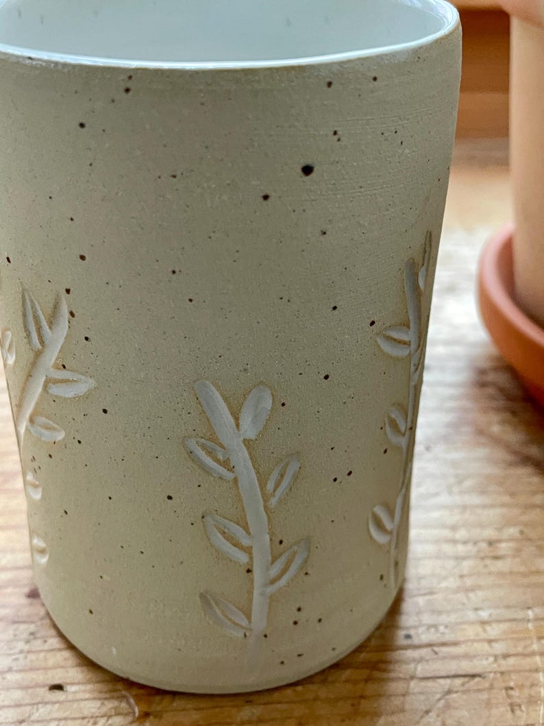 Pu&ograve; includere: Un bicchiere in ceramica beige con interno bianco ed esterno strutturato. Il bicchiere presenta un design a foglie intagliate. La superficie macchiata aggiunge un tocco rustico alla ceramica fatta a mano. Il bicchiere &egrave; adatto per bevande calde o fredde.