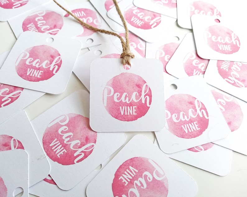 Puede incluir: Un mont&oacute;n de etiquetas de regalo cuadradas blancas con un c&iacute;rculo de acuarela rosa y el texto "Peach Vine" en blanco. Las etiquetas est&aacute;n esparcidas sobre una superficie blanca.