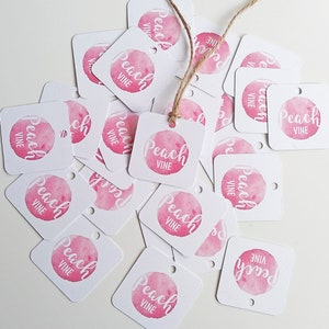 Puede incluir: Un mont&oacute;n de etiquetas de regalo cuadradas blancas con c&iacute;rculos de acuarela rosa y el texto "Peach Vine" en escritura blanca.