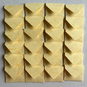 May include: A grid of sixteen small, square envelopes arranged in four rows and four columns. Each envelope is made of light yellow paper with a subtle, mottled, fibrous texture throughout, featuring a triangular flap folded downward.