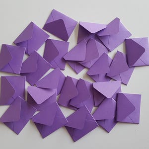 May include: A pile of purple envelopes, scattered on a white surface. The envelopes are all the same size and shape, and they are arranged in a random pattern.