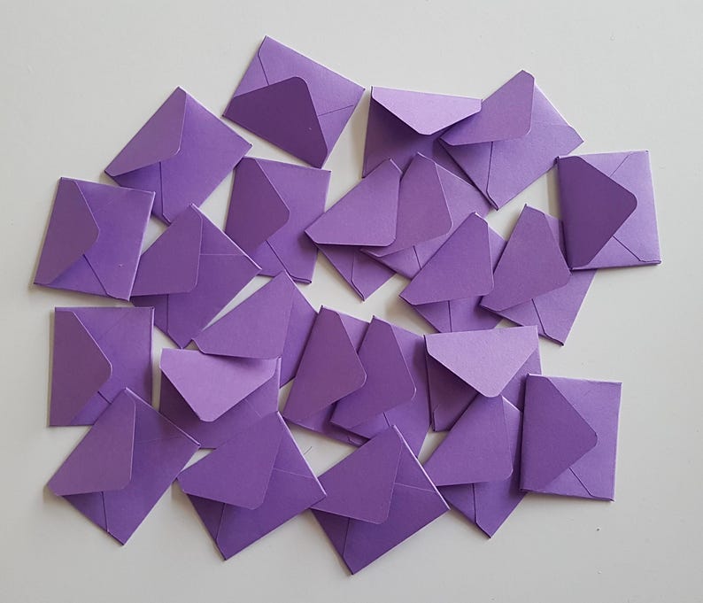 May include: A pile of purple envelopes, scattered on a white surface. The envelopes are all the same size and shape, and they are arranged in a random pattern.