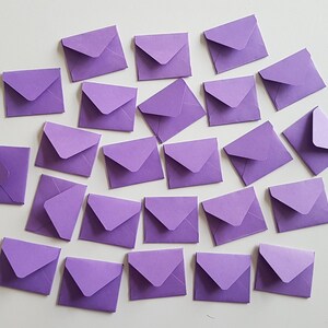 May include: A collection of 25 purple envelopes of various sizes, arranged in a random pattern on a white surface.