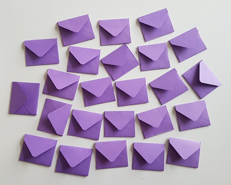 May include: A collection of 25 purple envelopes of various sizes, arranged in a random pattern on a white surface.