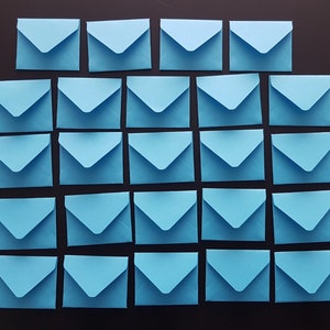 May include: A collection of 30 light blue envelopes arranged in a grid pattern on a black surface.