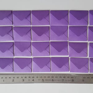 May include: A set of 25 purple envelopes arranged in a grid pattern. The envelopes are all the same size and have a slightly darker shade of purple on the flap.