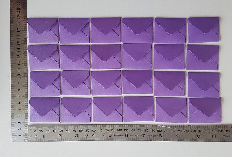 May include: A set of 25 purple envelopes arranged in a grid pattern. The envelopes are all the same size and have a slightly darker shade of purple on the flap.