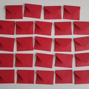 May include: A collection of twenty-one small, square, red envelopes arranged on a white surface. Each envelope is sealed and has a triangular flap. The envelopes are evenly spaced and create a visually appealing pattern.