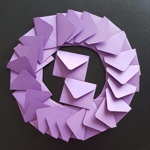 May include: A circle of lavender envelopes arranged in a circular pattern on a black background.