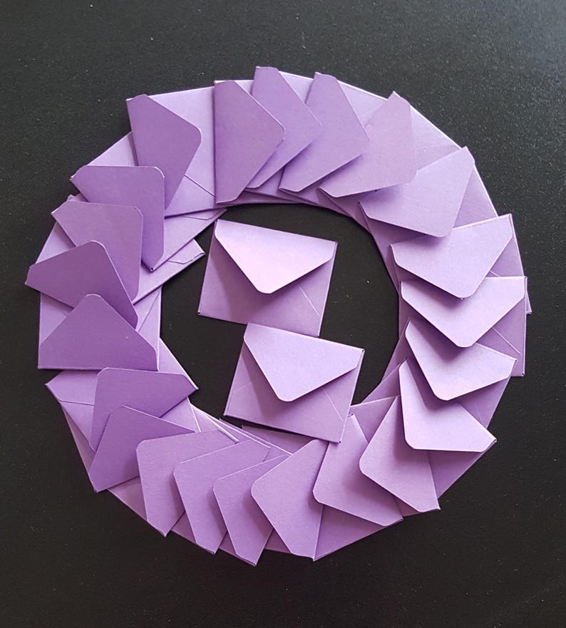 May include: A circle of lavender envelopes arranged in a circular pattern on a black background.
