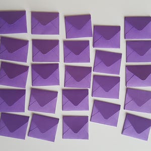 May include: A collection of 24 purple envelopes, arranged in rows on a white surface. The envelopes are all the same size and shape, and they are all closed.