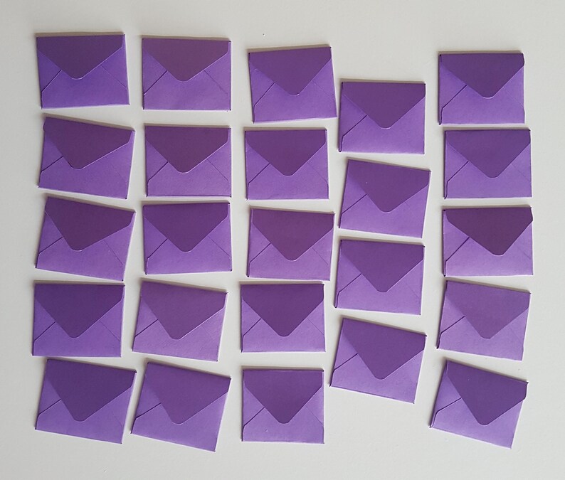 May include: A collection of 24 purple envelopes, arranged in rows on a white surface. The envelopes are all the same size and shape, and they are all closed.