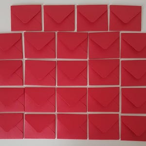 May include: Twenty-four small, square, red envelopes arranged in a grid. Each envelope has a classic folded design. The envelopes are evenly spaced and the bright red colour is consistent across all of them.