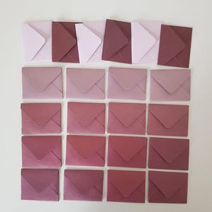 Puede incluir: Un surtido de pequeños sobres cuadrados en varios tonos de rosa y malva. Los sobres están dispuestos en un patrón de cuadrícula, mostrando un degradado de colores de claro a oscuro. Los sobres están cerrados y parecen ser de papel.