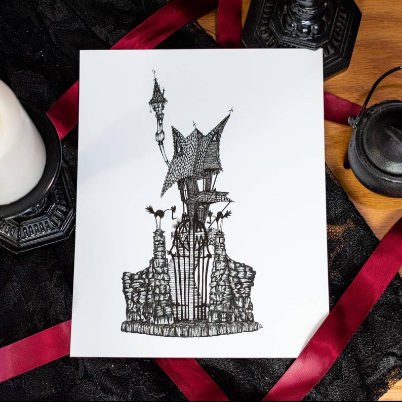 May include: A monochrome pen and ink drawing of a haunted house with a tall tower and a wrought iron gate. The artwork is on white paper, with a black lace and red ribbon background.