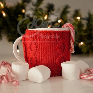 Puede incluir: Una taza blanca con un acogedor de punto rojo y un bastón de caramelo que sobresale de la parte superior. La taza está rodeada de malvaviscos blancos y bastones de caramelo sobre una superficie blanca.