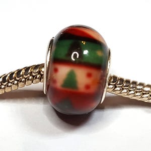 Könnte beinhalten: Ein weihnachtliches Charm-Bead mit einem rot, grün und weiß gehaltenen Design. Die Perle zeigt einen Weihnachtsbaum und ein Streifenmuster. Sie ist an einer silbernen Kette befestigt.