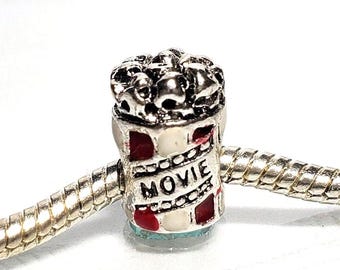 Puede incluir: Encanto de plata con un cubo de palomitas de maíz rojo y blanco con la palabra "MOVIE" en él. El encanto está en una cadena de plata.