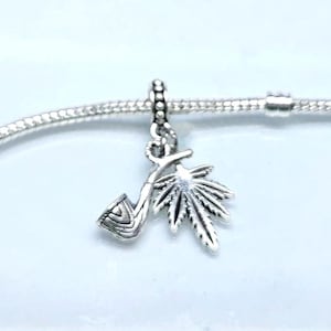 May include: A silver charm depicting a pipe and a cannabis leaf, suspended from a silver chain. The pipe has a curved stem and bowl. The cannabis leaf is intricately detailed. The charm is likely made of sterling silver and is suitable for a bracelet or necklace.