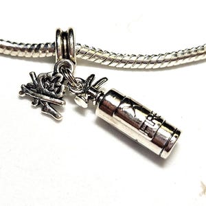 Könnte beinhalten: Ein silbernes Armband mit zwei Anhängern: ein Miniatur-Lagerfeuer und ein Feuerlöscher. Die Anhänger sind an einem silbernen Schlangenkettenarmband befestigt. Die Anhänger sind detailliert und haben einen Vintage-Look.