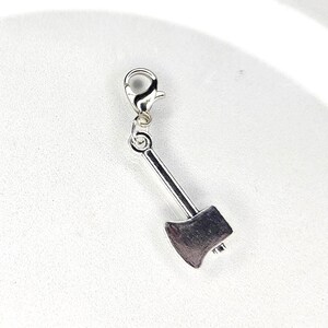 以下が含まれることがあります： ロブスタークラスプ付きの銀色の斧チャーム。斧の頭は詳細で、チャームはブレスレットやネックレスに取り付けるように設計されています。チャームは光沢のある金属製です。