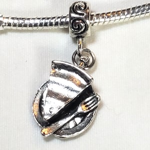 May include: Silver charm for a charm bracelet featuring a slice of pie on a plate with a fork.