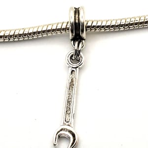 May include: Silver-colored wrench charm pendant. The charm is suspended from a silver-colored chain. The wrench is a detailed miniature, with a textured surface. The charm is designed to be a pendant or a charm for a bracelet.