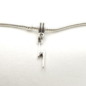 Op de afbeelding: Een zilveren bedel in de vorm van een bliksemschicht hangt aan een zilveren ketting. De bedel is gedetailleerd en heeft een gepolijste afwerking. De achtergrond is wit.