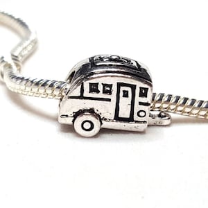 May include: Silver charm in the shape of a camper van with black detailing. The charm is on a silver chain.