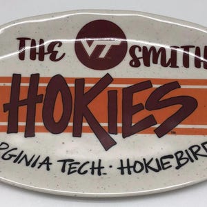 May include: Oval ceramic platter with a speckled cream background. The platter features the words "THE SMITHS" and "HOKIES" in maroon, with orange stripes and the text "VIRGINIA TECH. HOKIEBIRD" in black.