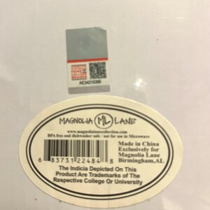 Op de afbeelding: Een wit productlabel met de tekst "MAGNOLIA ML LANE" in een zwarte ovaal. Het label bevat een barcode, websiteadres en tekst die aangeeft dat het product BPA-vrij en vaatwasmachinebestendig is. Een kleinere sticker bevindt zich boven het label.