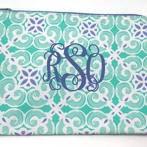May include: A rectangular zippered pouch with a teal, white, and purple geometric pattern. The pouch features a large, dark blue monogram of the letters RSO. A small tag is attached to the zipper.