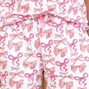 May include: White pajama shorts with a pink bow print. The shorts have a drawstring waist and a relaxed fit.