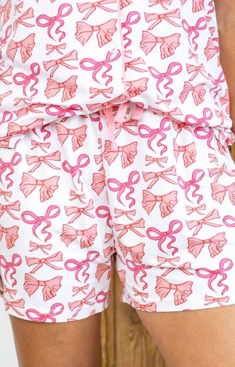 May include: White pajama shorts with a pink bow print. The shorts have a drawstring waist and a relaxed fit.
