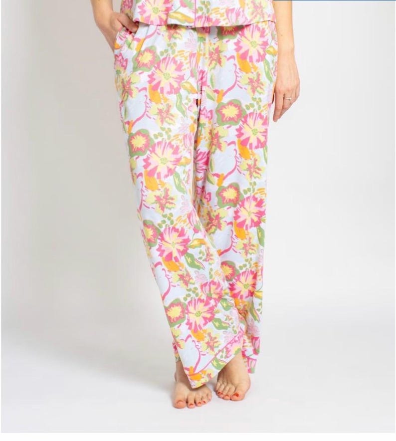 May include: Floral pajama pants in a light blue background with large pink, yellow, and orange flowers. The pants have a relaxed fit and a white trim. The image shows the pants from the waist down.