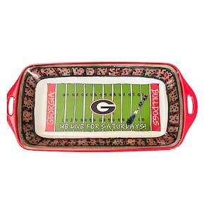 May include: A rectangular serving tray with a red border and handles. The interior features a green football field design with yard lines, the Georgia Bulldogs logo, and the text "WE LIVE FOR SATURDAYS!" and "BULLDOGS".