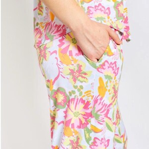 May include: A light blue floral print pajama set. The set features a vibrant pattern of pink, yellow, and green flowers. The person's hand is in the pocket of the pajama pants. The pajama top is visible.