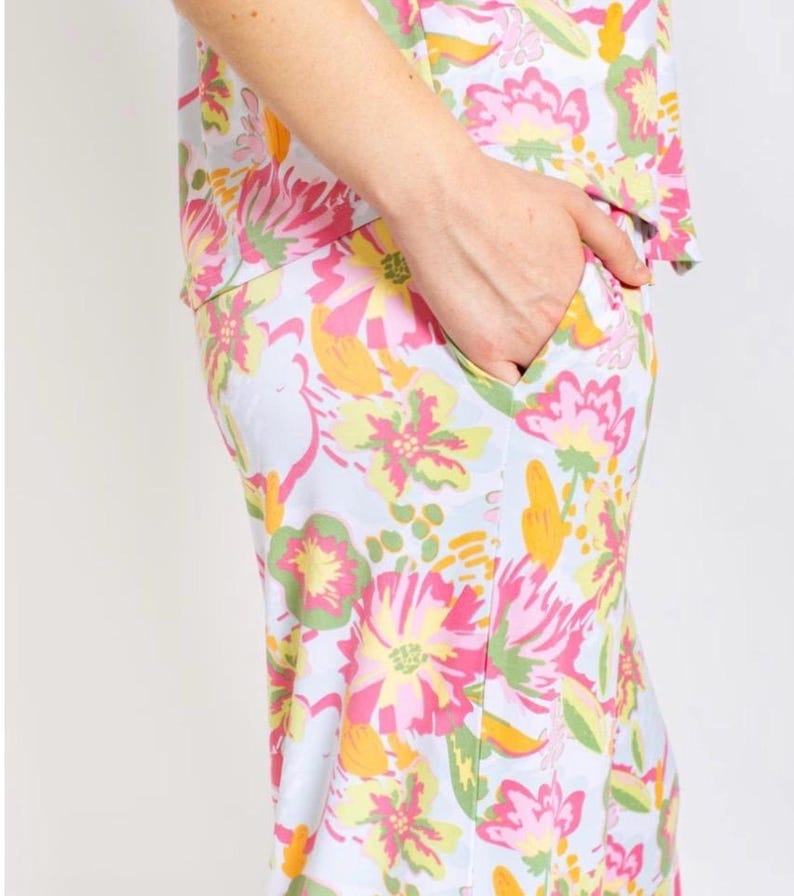 May include: A light blue floral print pajama set. The set features a vibrant pattern of pink, yellow, and green flowers. The person's hand is in the pocket of the pajama pants. The pajama top is visible.