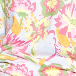 May include: Close-up of a fabric with a floral pattern. The design features large flowers in shades of pink, yellow, and green, set against a light blue background. The fabric has a soft, flowing appearance, suggesting it might be used for clothing or home decor.